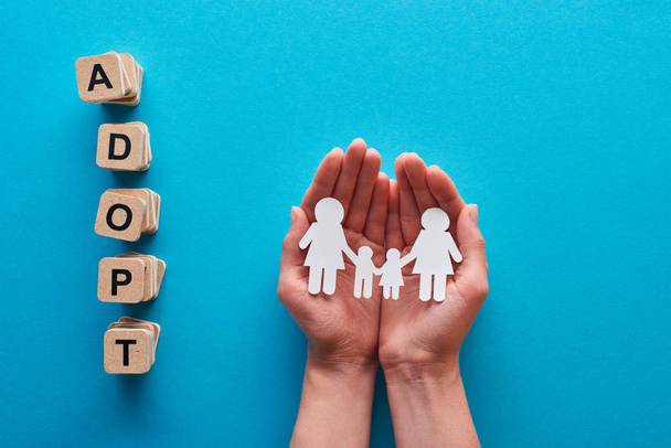 cropped view of woman holding paper cut lesbian family near blocks with adopt lettering on blue background - Photo, Image