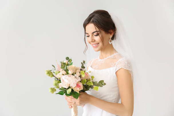 Beautiful young bride with bouquet of flowers on light background - Photo, Image