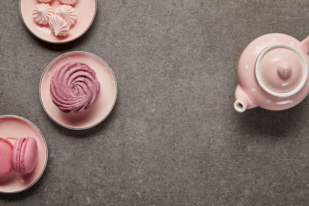 Top view of pink with dotted teapot and saucers with meringues and zephyr on gray background - Fotografie, Obrázek