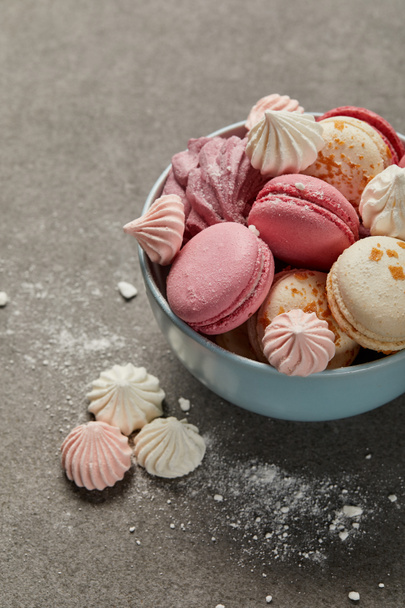 Cuenco azul con deliciosos macarrones franceses, suave zephyr y pequeños merengues rosados y blancos con migajas sobre fondo gris
 - Foto, imagen