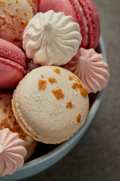 Delicious french macaroons, soft zephyr and small pink and white meringues in blue bowl on gray background - Foto, Bild