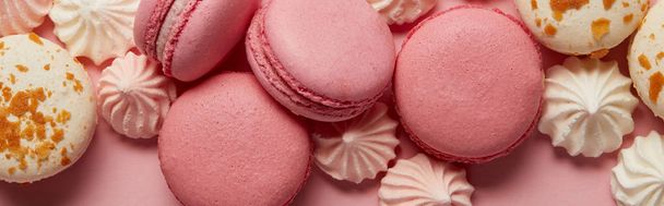 Deliciosos macarrones surtidos con pequeños merengues rosados y blancos sobre fondo rosado
 - Foto, imagen