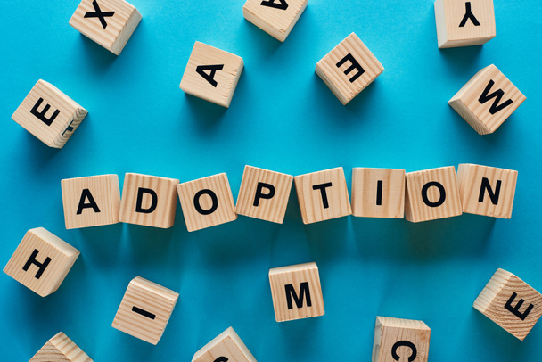 top view of adoption word made of wooden cubes on blue background - Foto, imagen
