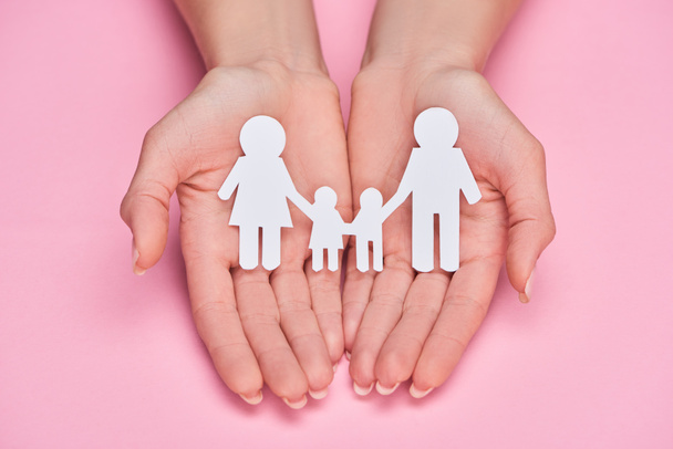 cropped view of woman holding paper cut family on pink background - Fotó, kép