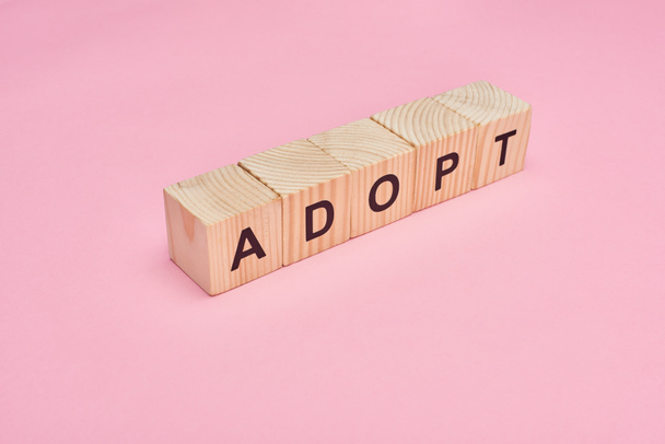 wooden cubes with adopt lettering on pink background - Foto, immagini