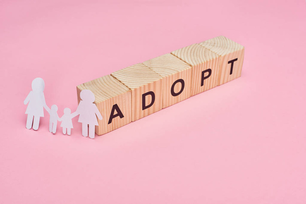 wooden cubes with adopt lettering and paper cut lesbian family on pink background - 写真・画像