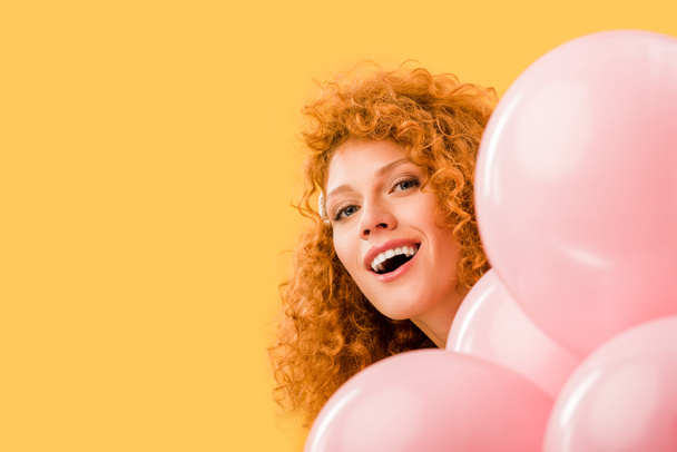 cheerful redhead woman with pink balloons isolated on yellow - Zdjęcie, obraz