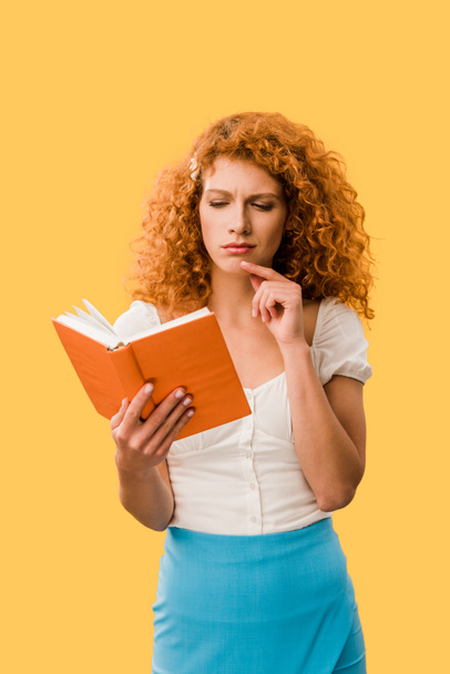 pensive redhead woman reading book isolated on yellow - Fotó, kép