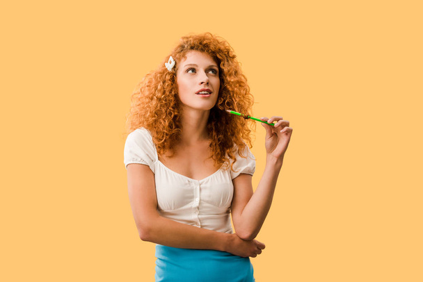黄色に隔離された鉛筆を持つ思慮深い赤毛の女性 - 写真・画像