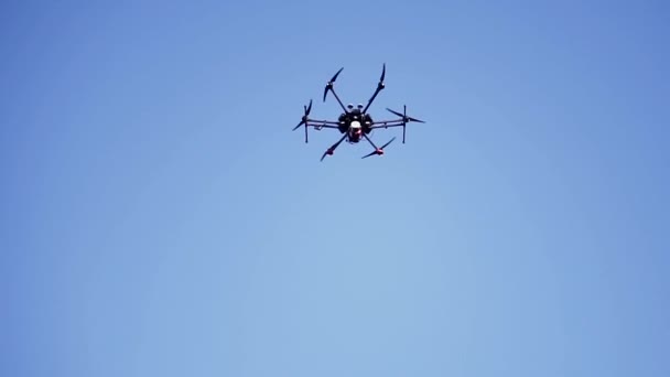 Czarny dron lecący pod błękitnym niebem z wirującymi ostrzami, widok z dołu. Klip. Kompaktowy quadcopter sterowany bezprzewodowymi zdalnymi nagraniami wideo i zdjęciami. - Materiał filmowy, wideo