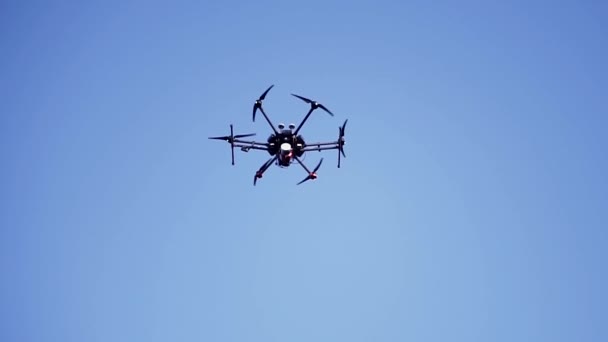 Zwarte drone vliegt tegen de blauwe lucht met draaiende bladen, onderaanzicht. Een knip. Compacte quadcopter bestuurd door draadloze remote shooting video footages en foto 's. - Video