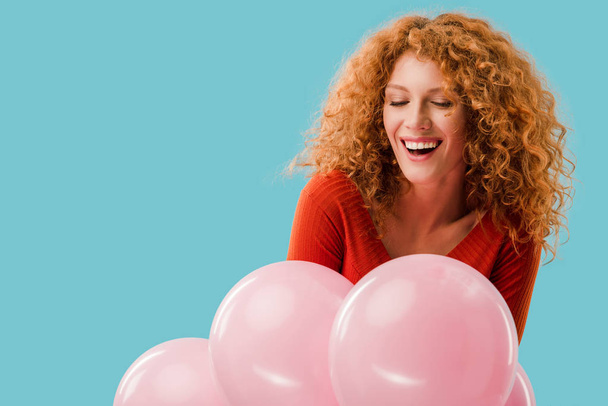 smiling redhead girl with pink balloons isolated on blue - Fotó, kép
