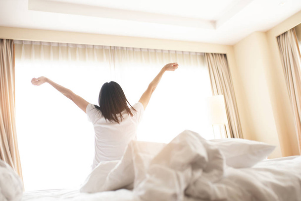 Vrouw die zich uitstrekt in bed na het wakker worden, achteraanzicht. Vrouw Sittin - Foto, afbeelding