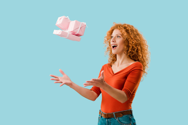 excited redhead girl throwing up gifts isolated on blue - Фото, зображення