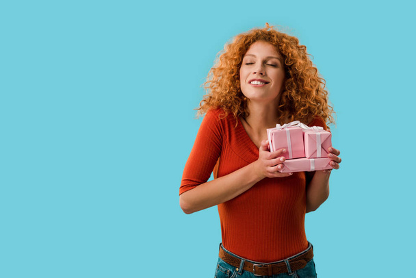 happy curly girl holding gifts isolated on blue - Zdjęcie, obraz
