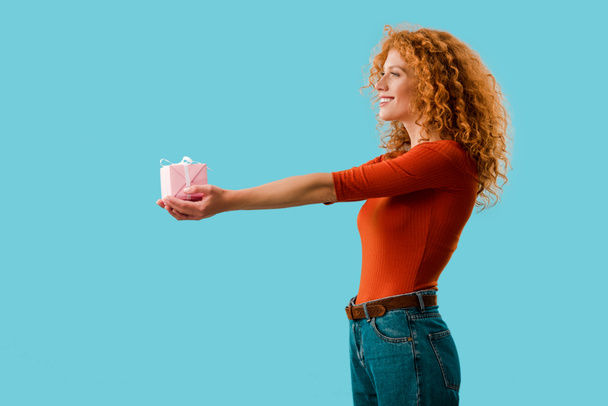 beautiful curly woman holding gift box isolated on blue - 写真・画像