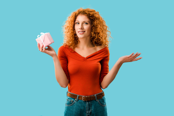 smiling curly woman with gift box isolated on blue - Φωτογραφία, εικόνα