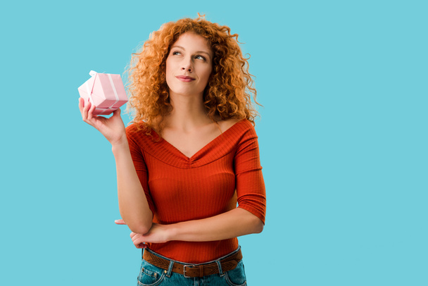 pensive redhead woman with gift box isolated on blue - Foto, imagen