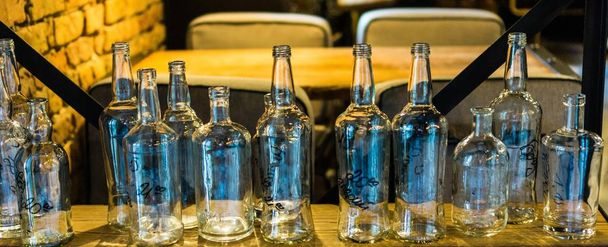 Botellas de vidrio de diferentes tamaños de pie sobre una mesa de madera en un elegante restaurante interior
 - Foto, Imagen