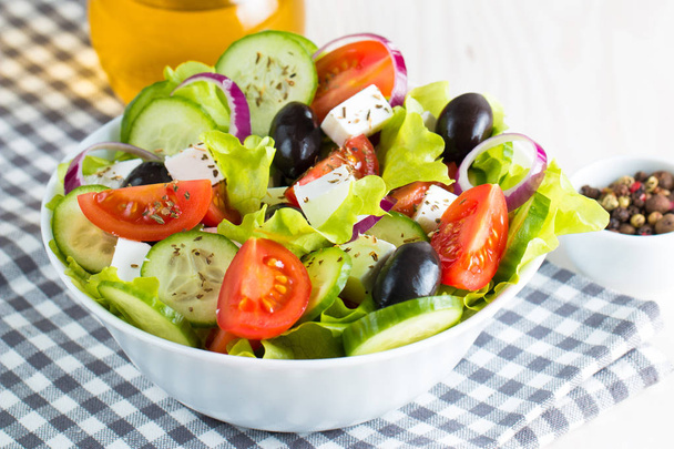 Fresh Greek salad made of cherry tomato, ruccola, arugula, feta, olives, cucumbers, onion and spices. Caesar salad in a white bowl on wooden background. Healthy organic diet food concept. - Photo, Image