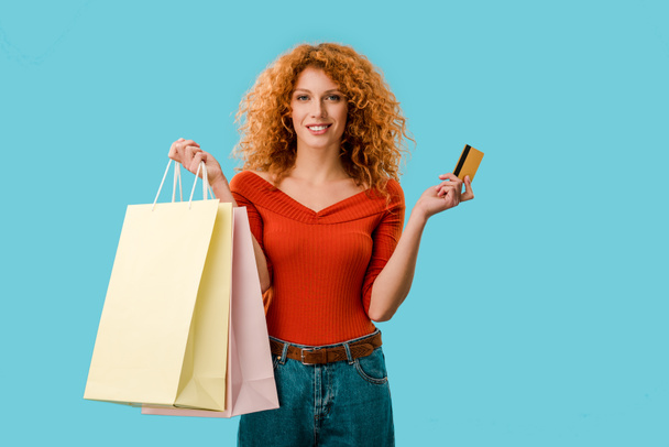 sorrindo mulher segurando sacos de compras e cartão de crédito, isolado em azul
 - Foto, Imagem