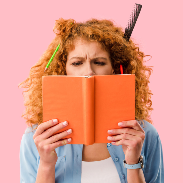 сфокусований студент з олівцями в книзі тримає волосся ізольовано на рожевому
 - Фото, зображення