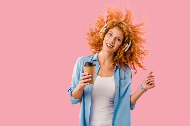 glückliche Frau mit Kaffee zum Tanzen und Musik hören in Kopfhörern, isoliert auf rosa - Foto, Bild