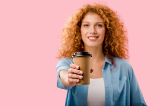 行くためにコーヒーを保持する赤い髪を持つ美しい巻き毛の女性の選択的な焦点, ピンクに隔離 - 写真・画像