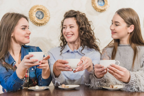 Three women friends enjoy coffee in the cafe. Enjoy coffee while chatting in the cafe. Young and beautiful girls with long blackheads. - Фото, изображение