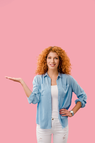 attractive redhead woman presenting something isolated on pink - Foto, afbeelding
