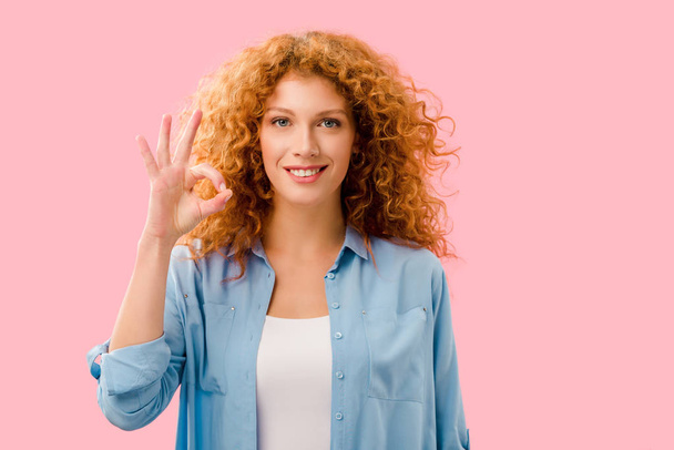 cheerful redhead girl showing ok sign isolated on pink - Фото, изображение