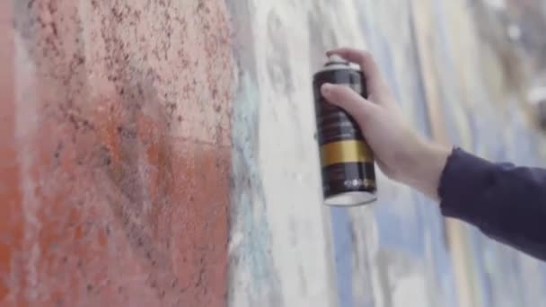 Tenendo in mano una bomboletta spray e disegnando graffiti colorati sul muro, concetto di street art. Azione. Vista laterale di un artista che dipinge con spray aerosol sulla parete, lavori di pittura su calcestruzzo
. - Filmati, video