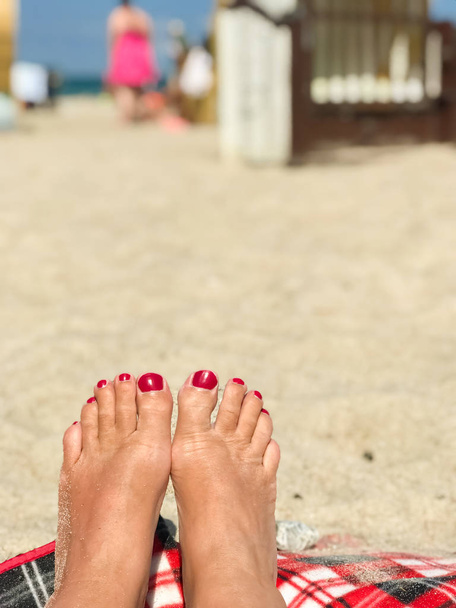 Frauenfüße mit rotem Nagellack am Strand, im Hintergrund Strandkörbe und blauer Himmel - Foto, Bild