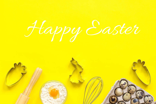 Happy Easter text and rolling pin, whisk for whipping, cookie cutters, quail eggs flour on yellow paper background - Фото, изображение
