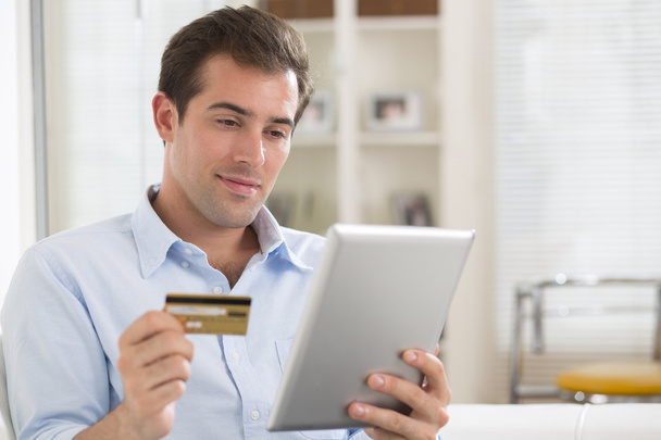 Portrait of young man holding tablet pc and credit card.indoor - Foto, afbeelding