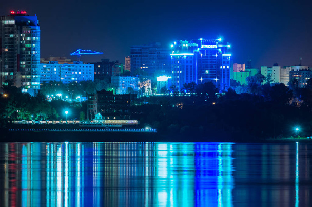 Nachtaufnahme der Stadt Chabarowsk vom Amur aus. blauer Nachthimmel. Die nächtliche Stadt ist hell erleuchtet mit Laternen. Pegel des Amur bei rund 159 Zentimetern. - Foto, Bild