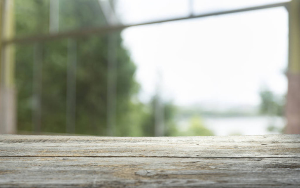 Άδειο ξύλινο τραπέζι επάνω στο θολώματος της κουρτίνας με θέα το παράθυρο πράσινο από το φόντο του κήπου δέντρο. Για την απεικόνιση του προϊόντος μοντάζ ή το κλειδί σχεδίασης οπτική διάταξη - Φωτογραφία, εικόνα