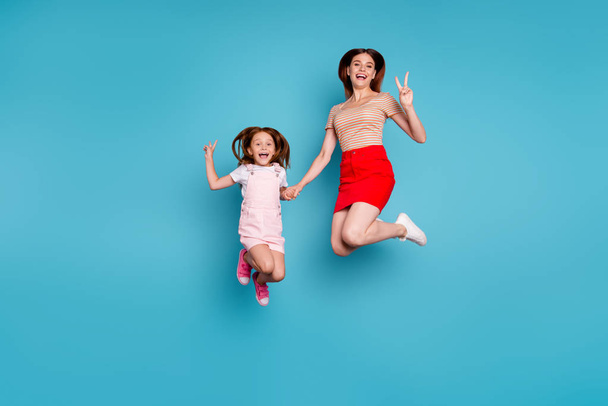 Full body photo of foxy little lady and mom showing v-sign symbols jumping high wear casual clothes isolated blue background - Фото, зображення