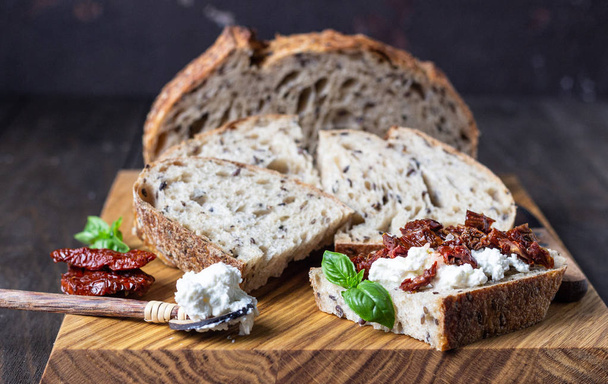 Bread slices with ricotta cheese, sun dried tomatoes and basil served on wooden cutting board. Bruschetta with ricotta cheese, dried tomatoes and basil.  - Fotoğraf, Görsel