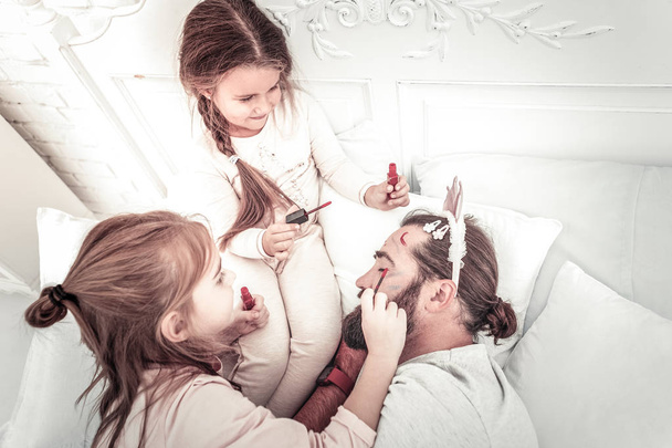 Szczęśliwy uśmiechnięty dziewcząt malarstwo na tatusiowie twarz podczas on drzemki - Zdjęcie, obraz