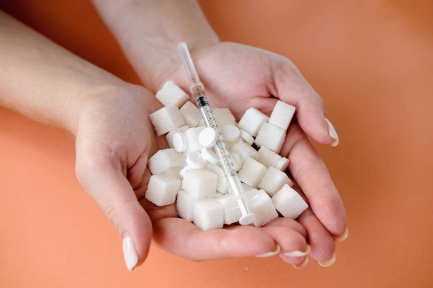Femme tenant des cubes de sucre blanc et une seringue d'insuline sur fond orange. Diabète, maladie du sucre, aliments malsains, concept de régime alimentaire. Espace de copie
 - Photo, image