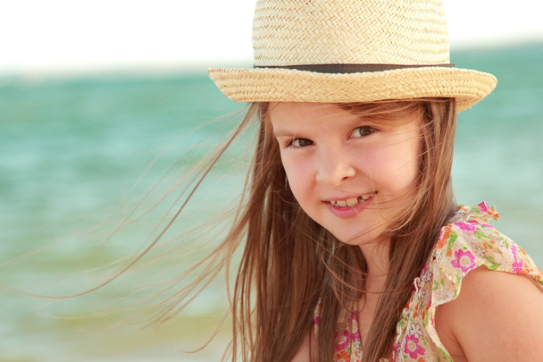 Portrait of a little girl who dreams of a hat on a background of a sea landscape outdoors. - Фото, изображение