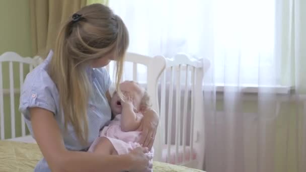 Mom cradles the baby on her hands. A woman is holding a little girl in her arms. Young mother with her daughter sitting on the bed. - Záběry, video