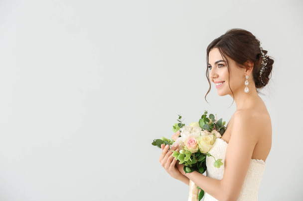 Hermosa novia joven con ramo de flores sobre fondo claro
 - Foto, Imagen