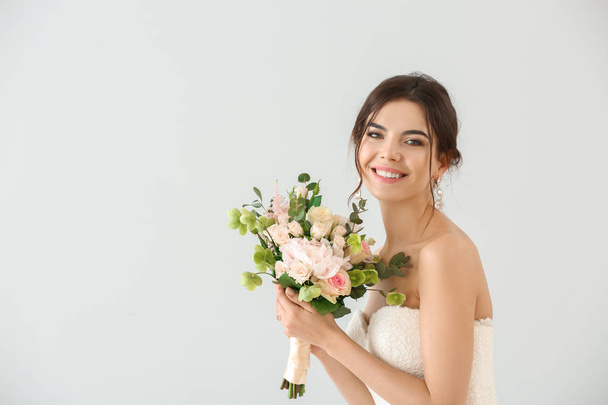 Gyönyörű fiatal menyasszony csokor virág a világos háttér - Fotó, kép