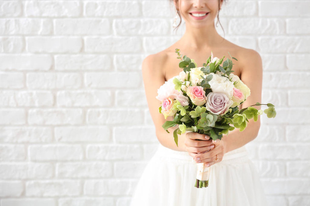 Beautiful young bride with bouquet of flowers on white brick background - Photo, Image