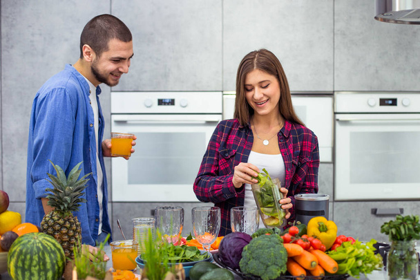 Desayuno saludable para una pareja joven por la mañana, hombre bebiendo jugo de naranja y señora preparando el batido en una cocina moderna
 - Foto, Imagen