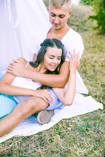 Lovely young couple in love in the summer in a field under a tree. Young couple enjoying each other in the summer on the nature - Foto, Imagen
