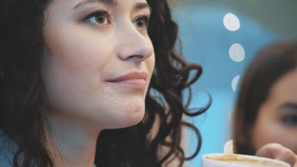 Young pretty girl sitting in a cafe. During this time it is a spoon of cappuccino. Enjoying a pleasant taste of coffee and calmness. - Imágenes, Vídeo