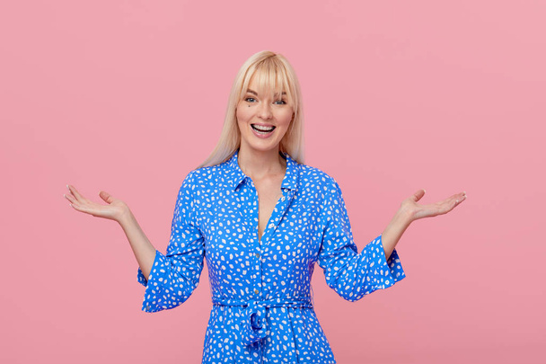 Woman surprise showing product. Beautiful girl with blond hair and braces pointing to the side . Presenting your product. Isolated on pink background. Expressive facial expressions. Wow emotions  - Foto, afbeelding